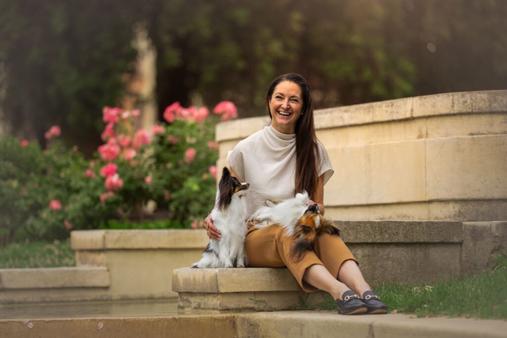 Nicole Laver smiling with two Papillons in a rose garden